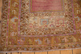 Corner of a distressed Oushak rug with saffron, purple, and blue meandering vine borders.