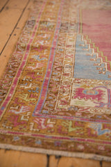 Angled view of the Oushak rug's prayer corner, showing saffron and purple meandering vine borders.