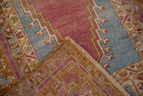Folded corner of a distressed Oushak rug showing the purple pile and hand-knotted ochre back.