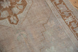 Distressed Oushak rug's stepped spandrel detail in muted pale bronze and antique ivory pile.
