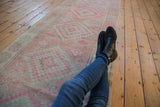 Muted pink, blush, and ivory geometric patterns of a distressed Oushak runner under crossed legs.