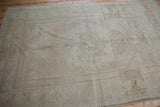 Distressed Oushak rug corner with aged beige field and faded ivory floral border design.