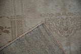 Distressed vintage Oushak rug showing hand-knotted back, original side selvage, and faded neutral patterns.