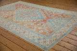 Angled view of a distressed Oushak carpet showing the soft blue and cinnabar geometric design.
