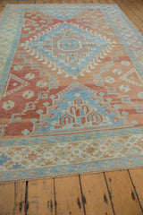 Angled perspective of a distressed Oushak carpet showing its geometric red and blue design.