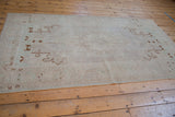 Angled view of a distressed Oushak rug with a tone-on-tone ivory field and brown spandrels.
