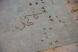 Evenly worn pile of a distressed Oushak rug showing brown motifs on a seafoam and ivory field.