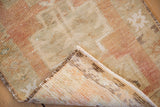Distressed vintage Oushak rug, corner folded showing worn beige geometric pile and woven brown back.