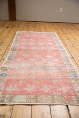Close-up of the distressed Oushak runner's faded pink pile, floral border, and intact selvage.