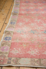 Distressed pink Oushak runner's faded floral field with worn texture and colorful border.