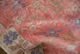 Distressed vintage Oushak rug runner showing faded pink and blue floral pattern, with worn pile and intact side cord.