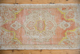 Corner of distressed Oushak mat, with coral peach, ivory, saffron yellow, and textured worn pile.