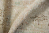 Distressed Oushak rug close-up: worn pile, visible knot heads, soft beige and seafoam tones.