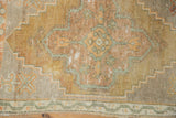 Distressed Oushak rug detail with stepped geometrics and plant motifs in gold, rust, and green.