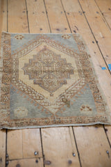 Distressed Oushak rug corner revealing stepped medallion, vine palmette border, and worn pile.