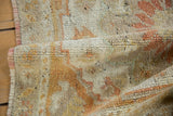 Visible knot heads and textured distressed pile of the Oushak rug, in ivory and pale terra cotta.