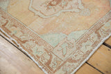 Distressed vintage Oushak rug corner showing beige pile, faint foundation, and its intact selvage.