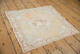 Distressed Oushak rug corner with faded floral detail in beige, apricot, and seafoam green.