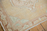 Distressed Oushak rug corner: mostly even wear on beige pile, copper border, intact fringe.