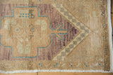 Distressed vintage Oushak rug corner, worn pile revealing foundation, beige and violet tones.