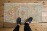 Distressed vintage Oushak rug mat in muted orange and beige with feet for scale.