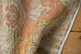 Folded vintage Oushak rug pile showing distressed orange, beige, and saffron with wear.