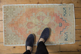 Softly colored distressed Oushak rug mat, apricot and beige geometric pattern, low pile, feet for scale.