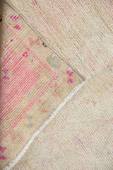 Folded corner of vintage Oushak rug shows distressed pale pink pile and striped beige, seafoam reverse.