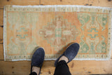 Distressed Oushak rug mat with pale orange and seafoam green motifs, showing even wear.