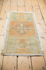 Distressed Oushak rug corner showing pale rust, seafoam green patterns, and worn pile.
