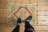 Feet on a vintage distressed Oushak rug, highlighting copper and sea foam green geometric elements.