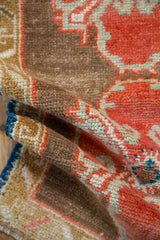Textured pile of a distressed Oushak rug, showing orange rust, brown, and pale bronze ram's horn motifs.