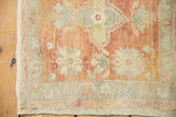 Distressed vintage Oushak corner shows intact selvage, knot heads, and seafoam floral vinery.