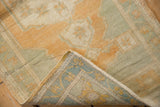 Curled distressed Oushak rug showing light gold and sage pile with its woven geometric back.