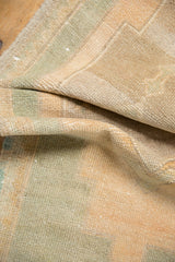 Close-up of distressed vintage Oushak rug showing pale apricot, seafoam abrashes, and wear.