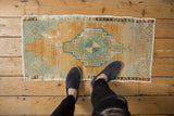 Distressed vintage Oushak rug corner, showing faded teal, orange, and ivory stepped geometric pattern.