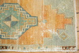 Oushak rug corner detail: distressed pile, geometric teal and golden orange stepped motifs.