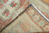 Oushak rug corner reveals distressed cochineal and seafoam pile, with visible striped foundation.