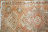 Distressed Oushak rug detail showing apricot and beige floral motifs with visible foundation.