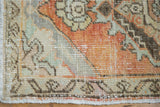 Fringe and distressed pile texture of an Oushak rug in muted rust, beige, and green tones.