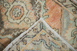 Distressed Oushak rug mat corner, showing worn pile with pale rust, beige, slate, and intact selvage.