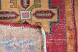 Distressed Oushak rug corner showing geometric pile, cherry red selvage, and faint woven foundation.