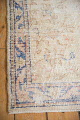 Distressed Oushak runner corner, ivory field, dusty blue border, visible knot heads, and selvage.