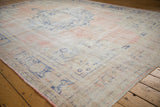 Distressed Oushak carpet corner, faded dusty rose, ivory, and pale blue worn motifs.
