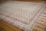 Distressed vintage Oushak carpet with faded red trellis pattern and starburst border.