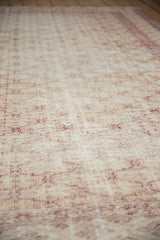 Distressed vintage Oushak carpet, its worn ivory and beige pile with faded red trellis.