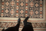Distressed Oushak rug detail showing geometric guls, stylized motifs, and cherry red pawn border pattern.