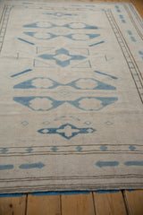 Textured vintage distressed Oushak rug, ivory field, geometric blue motifs, and brown outlines.