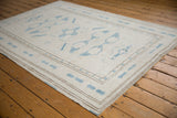 Distressed Oushak rug corner, showing worn texture, pale blue geometric relief, and thin border lines.
