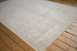 Corner of distressed Oushak carpet, showing faded plant motifs in ivory and beige tones.
